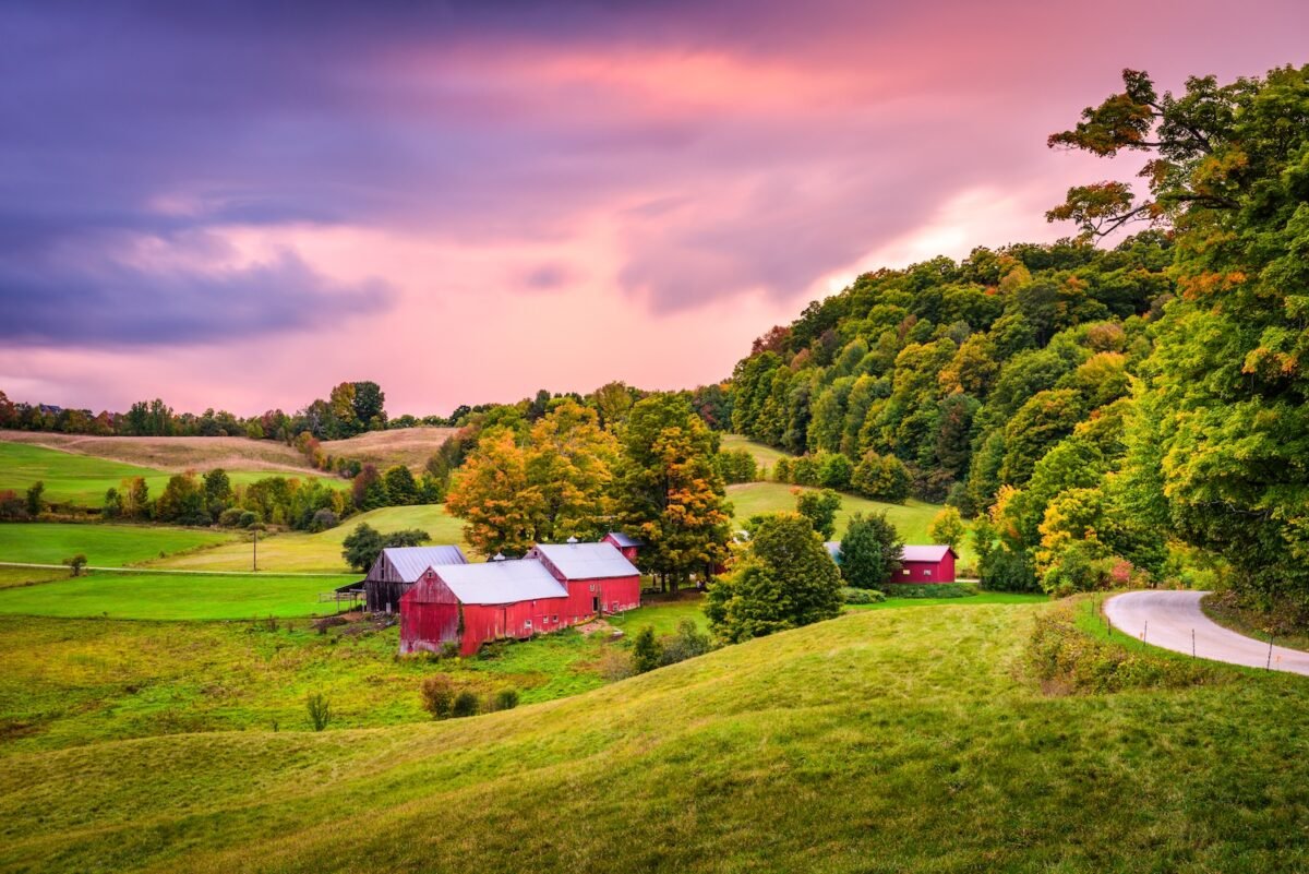 Red barns and rolling farmland surrounded by early fall foliage in rural Vermont